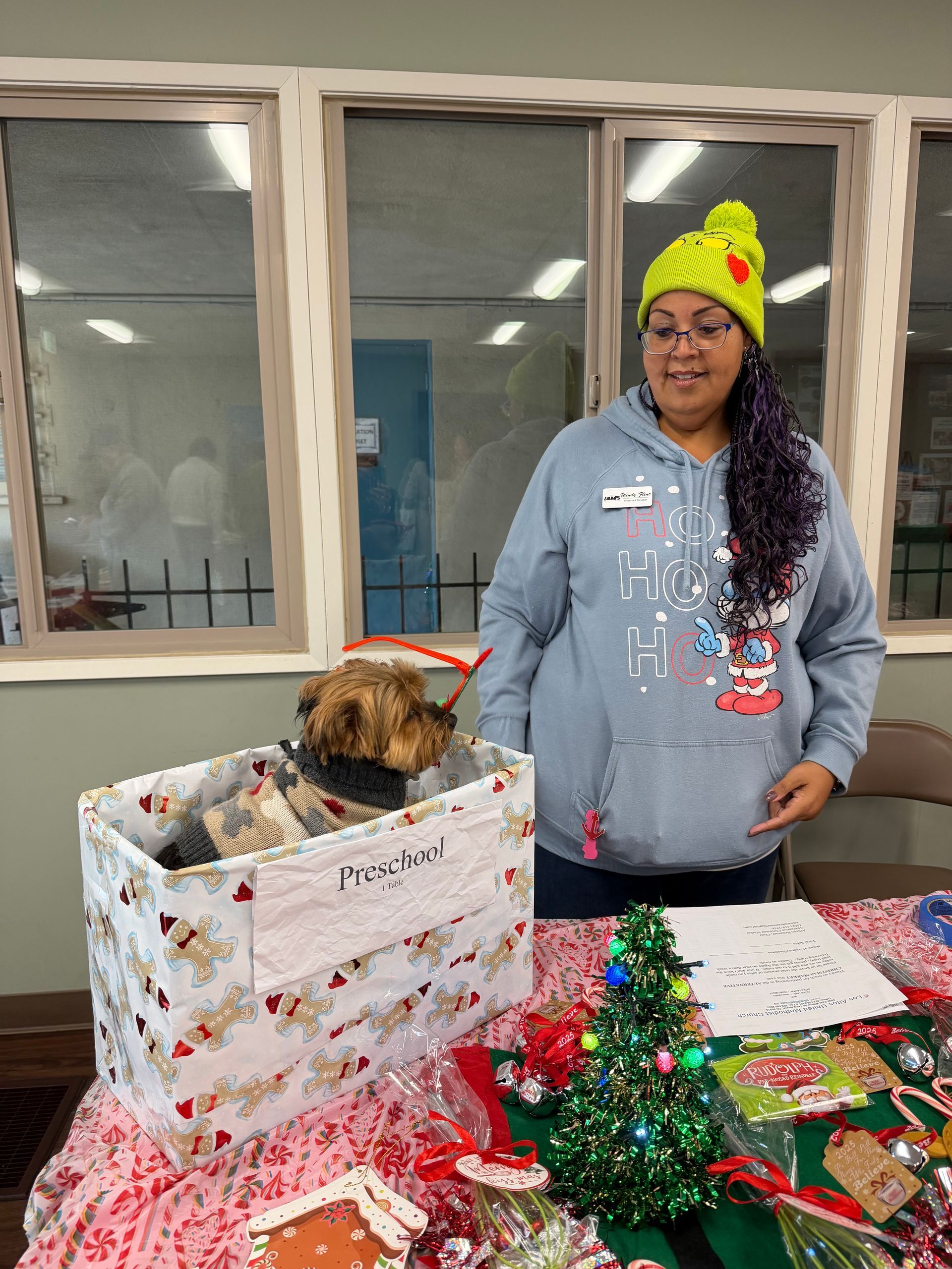 Person standing beside a decorated gift box and a small dog in a festive indoor setting
