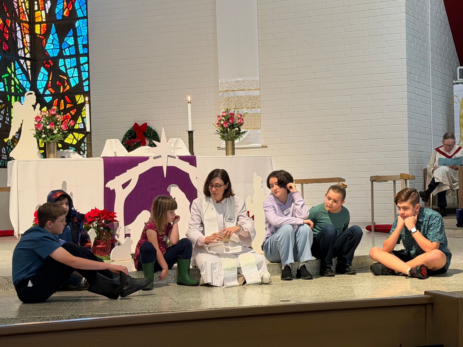Children seated on a church alter near the pastor, with candles and flowers and a stained glass window in the background Children seated on a church alter near the pastor, with candles and flowers and a stained glass window in the background