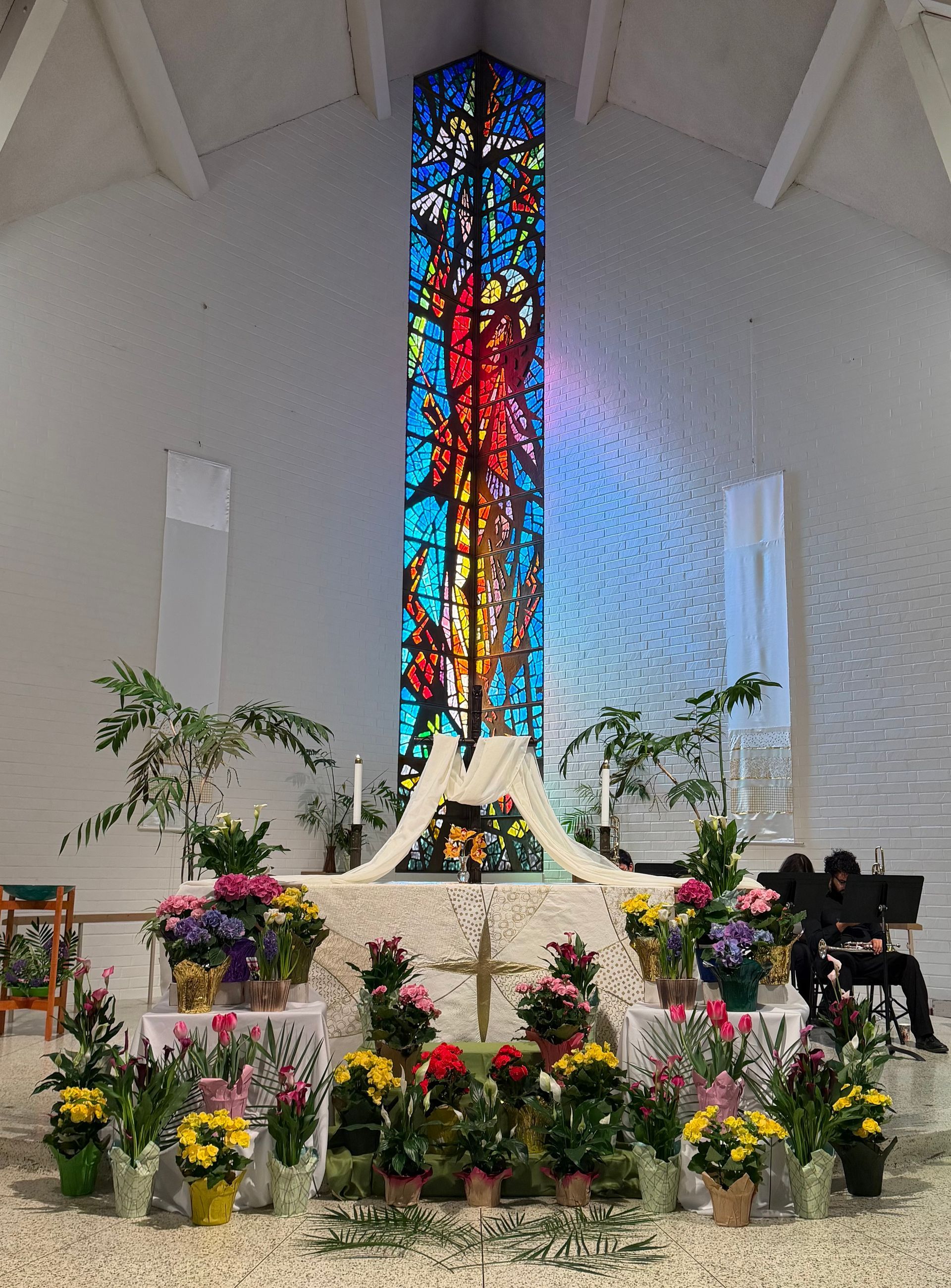 Church altar decorated with flowers before a tall stained-glass window in blue, red, and gold