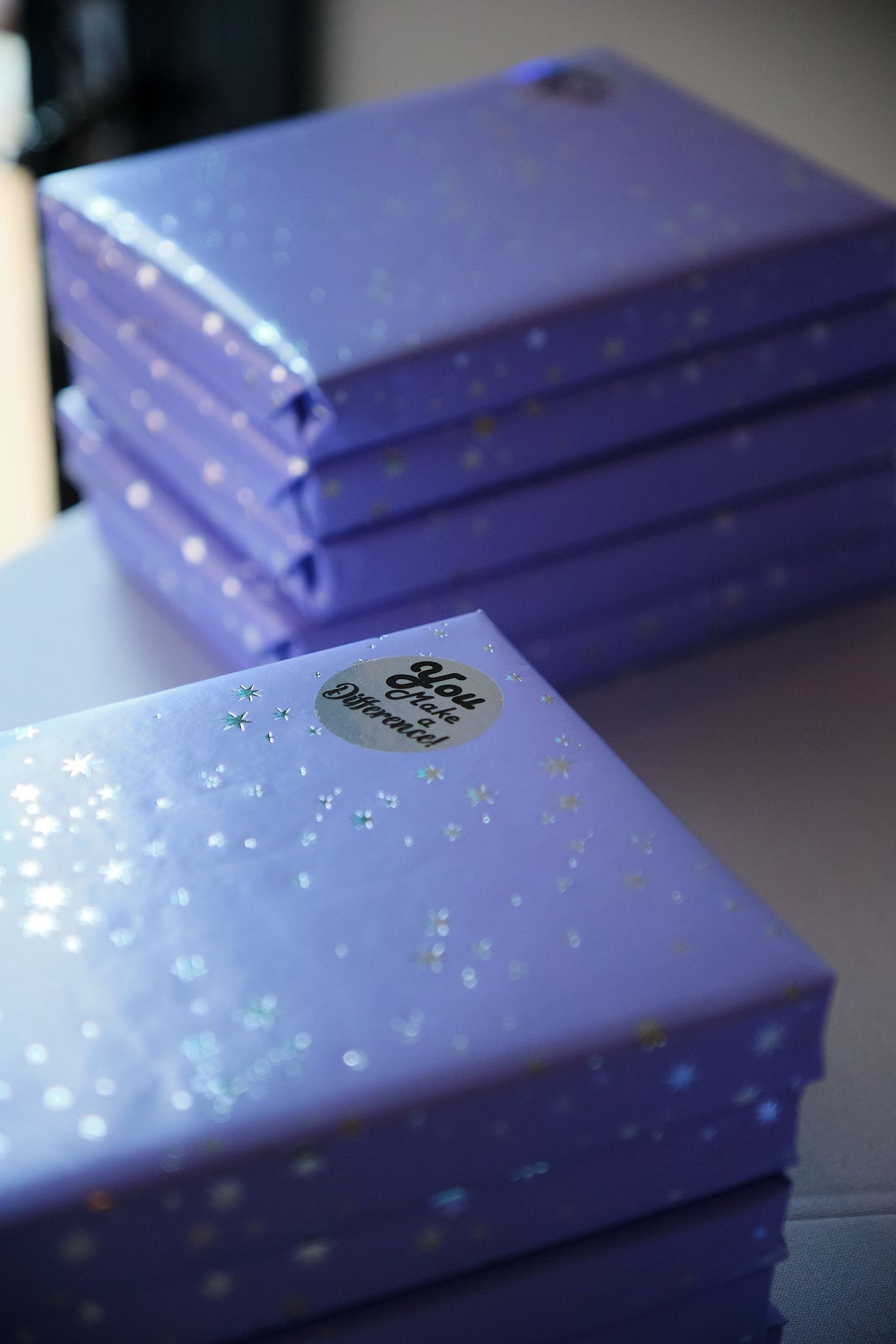 A stack of light purple boxes with a glittery star pattern and a circular sticker on the top box.