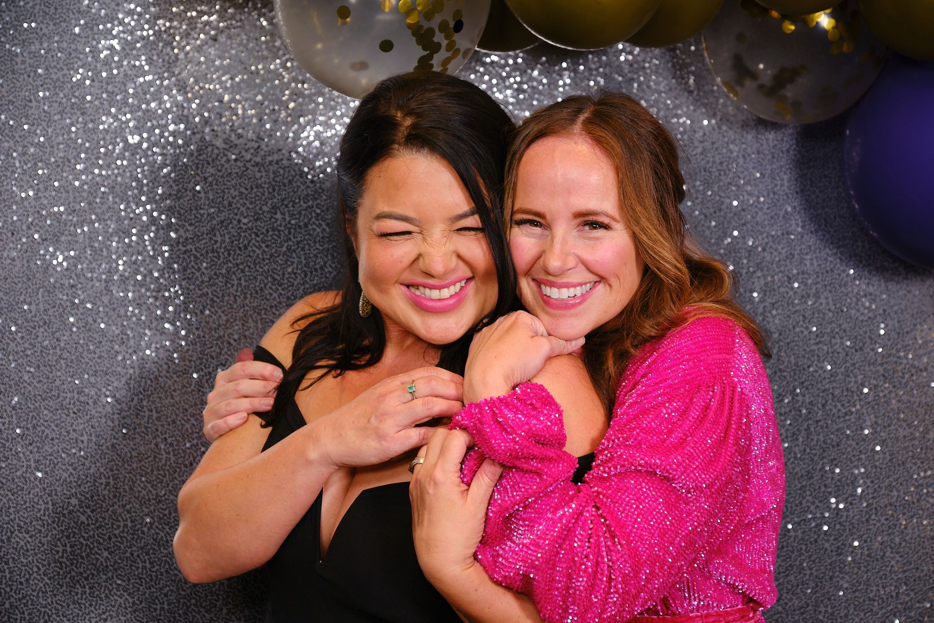 Two people smiling and hugging in front of a gray.