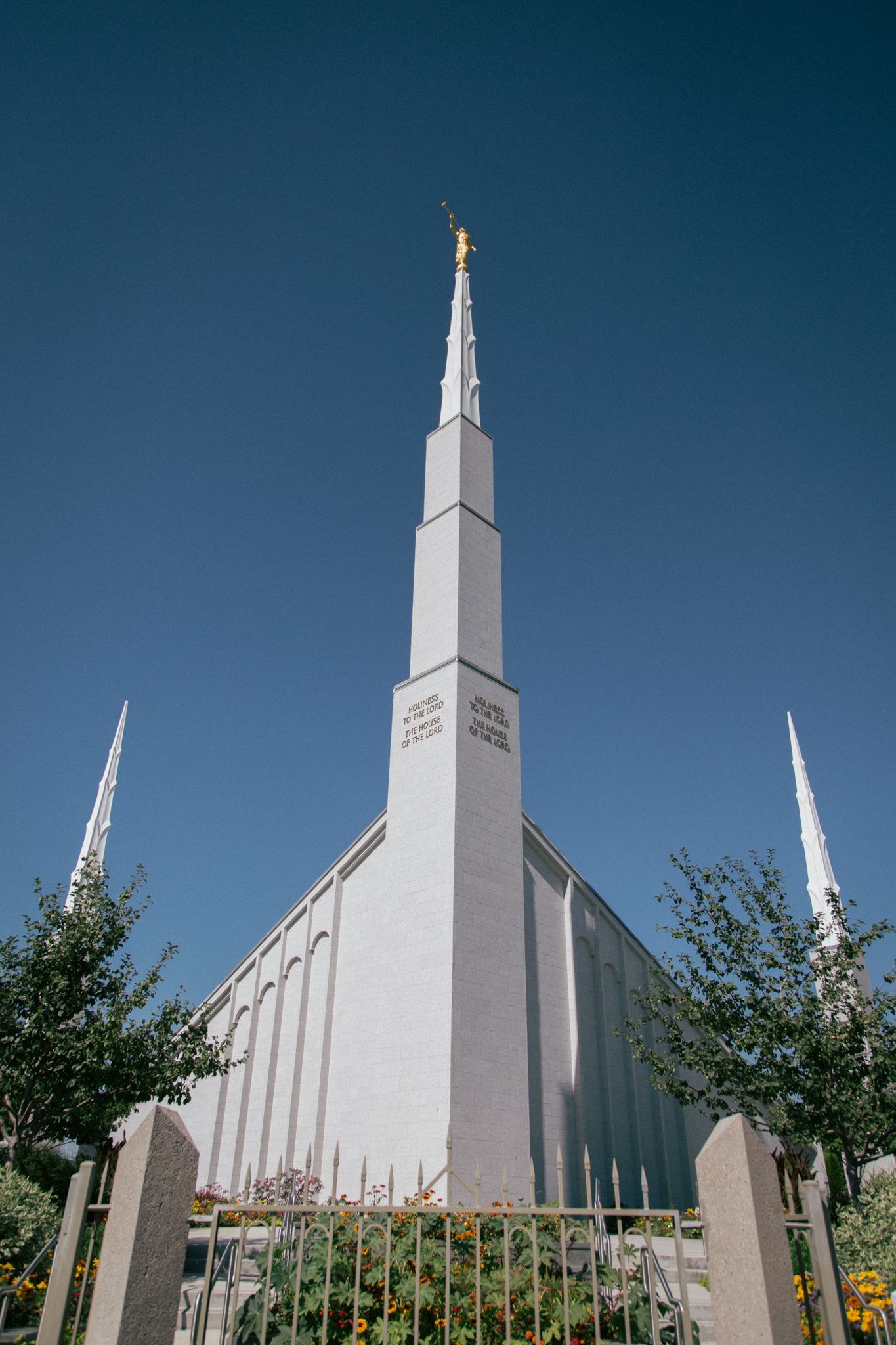 A white LDS temple with a tall central spire and a gold statue, set against a clear blue sky.