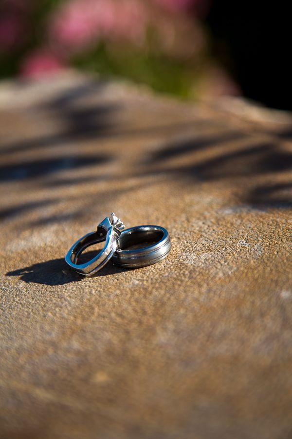 Two rings, one with a stone setting, resting on a rough stone surface with shadows cast nearby.