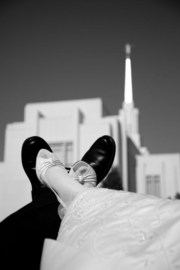 A black-and-white low-angle shot of a couple’s feet in formal attire resting in front of a church building with a steeple.