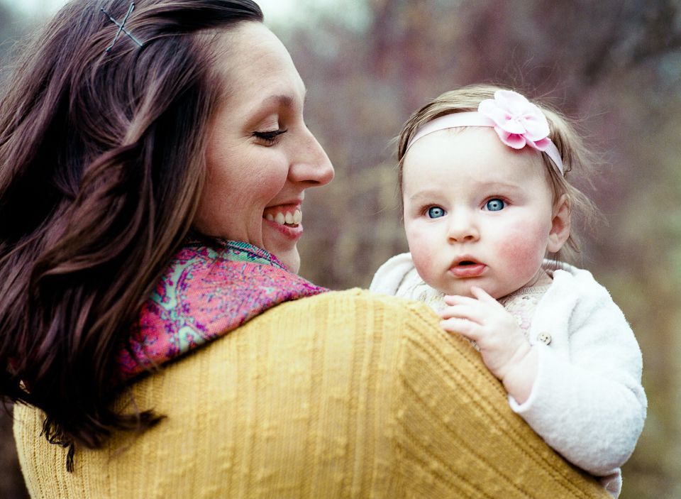 A person in a yellow sweater holds a baby wearing a white cardigan and a pink flower headband.