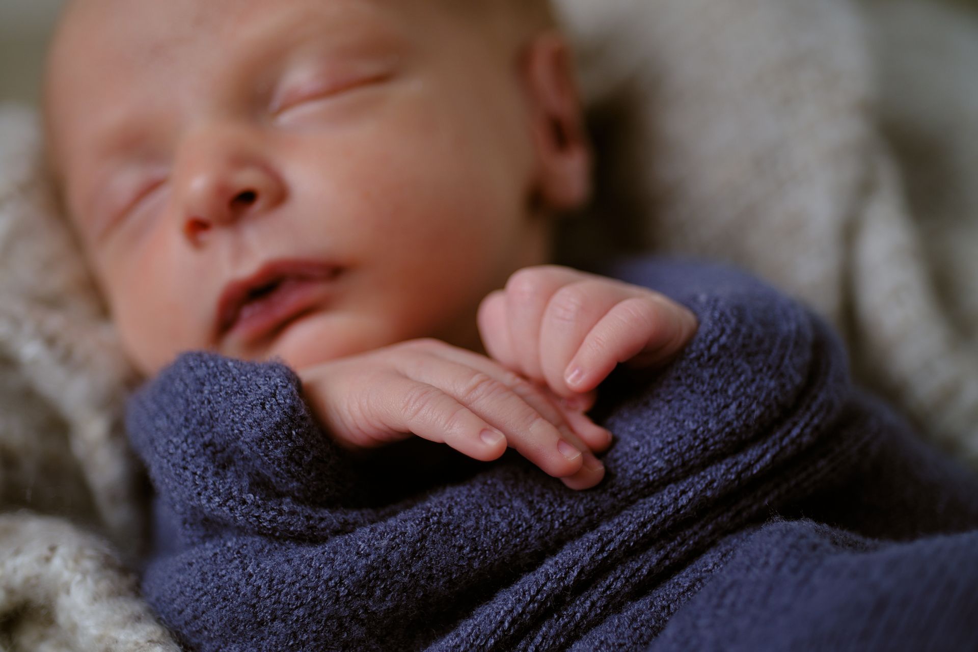 A swaddled infant sleeping peacefully with hands tucked near their chin.