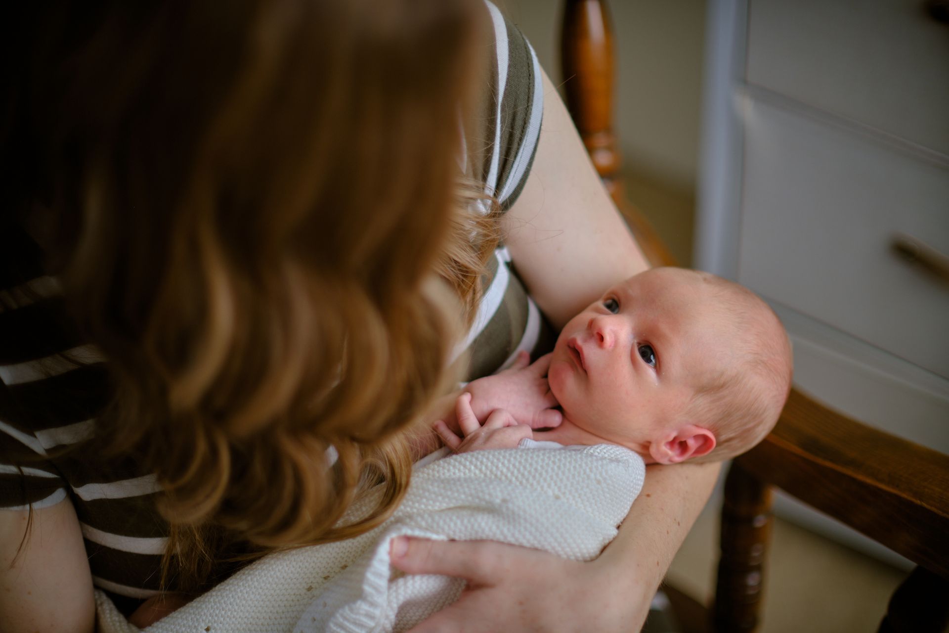 A person wearing a striped shirt holds a swaddled infant who is looking up toward them.