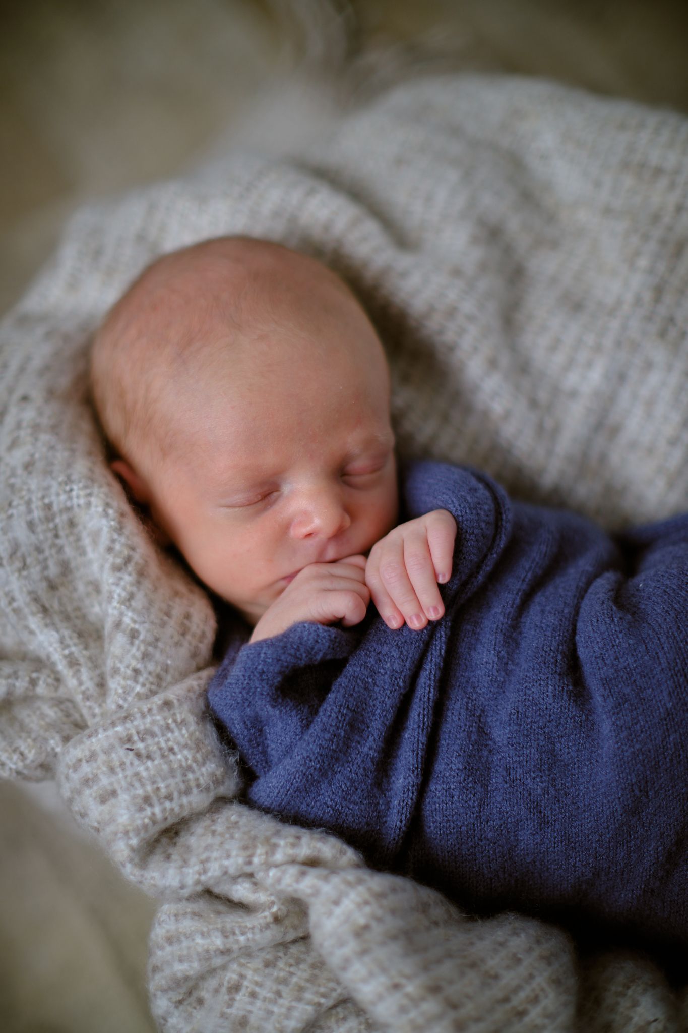 A sleeping newborn wrapped in a blue cloth, nestled in a soft, textured cream-colored blanket.