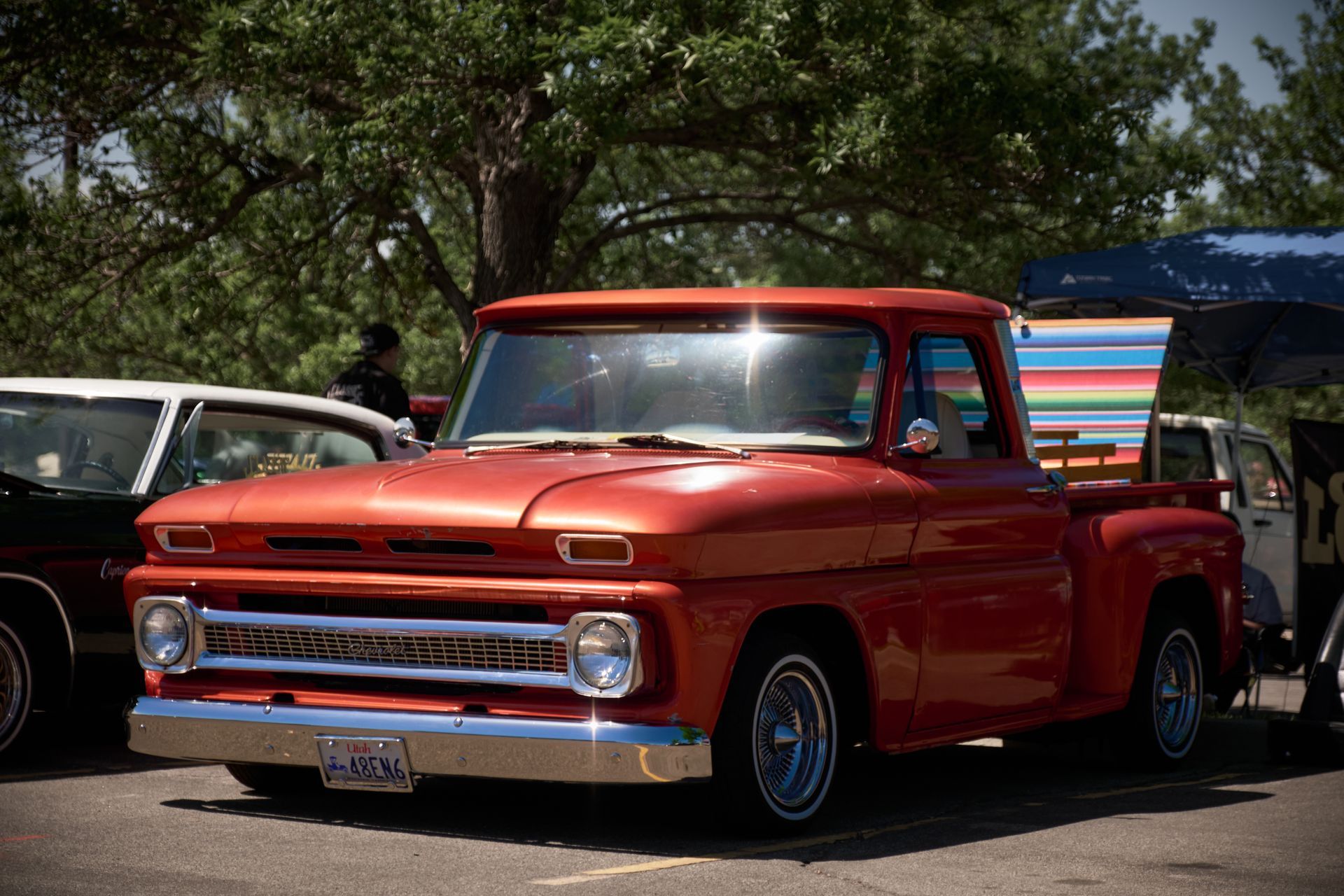 A bright orange vintage Chevrolet pickup truck parked on a sunny day at a car show.