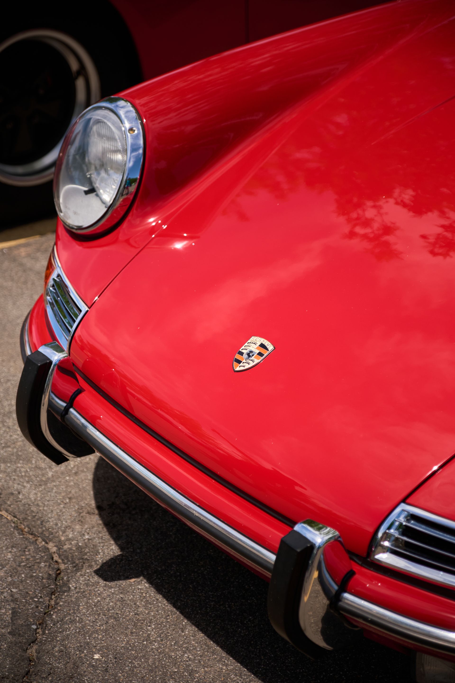 Close-up of the bright red front hood and chrome bumper of a vintage Porsche car parked on asphalt.