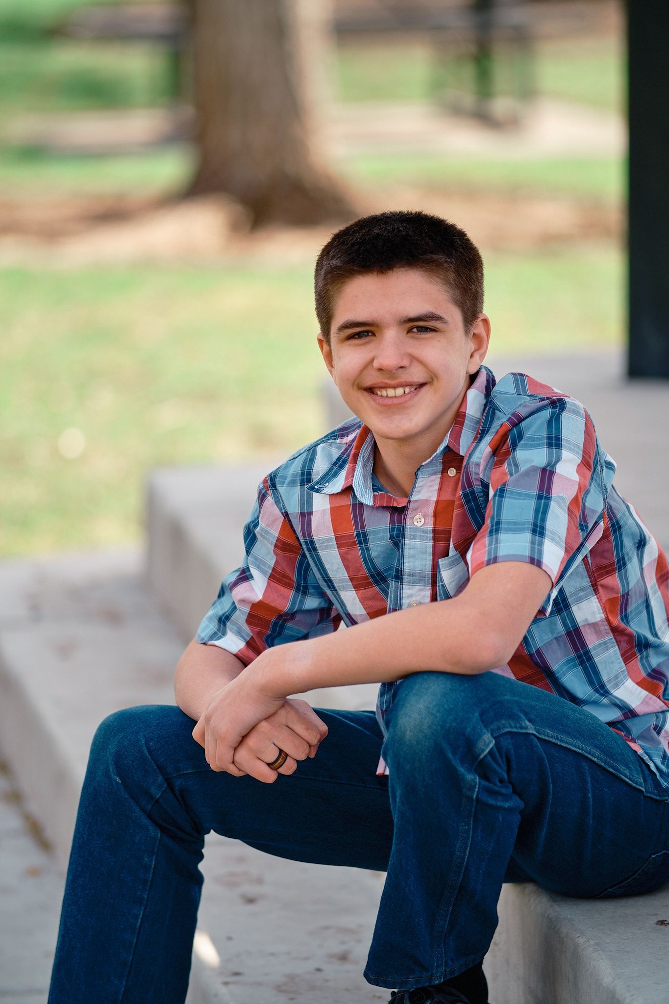 A person wearing a plaid shirt and jeans sitting on outdoor concrete steps, smiling toward the camera.