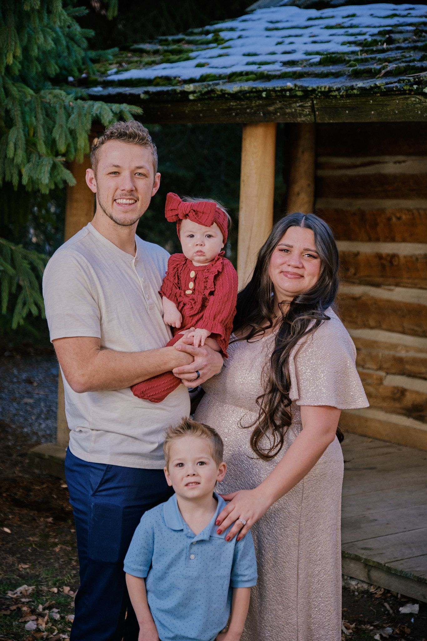 A family of four posing for a portrait outside a rustic wooden building, dressed in casual and formal attire.