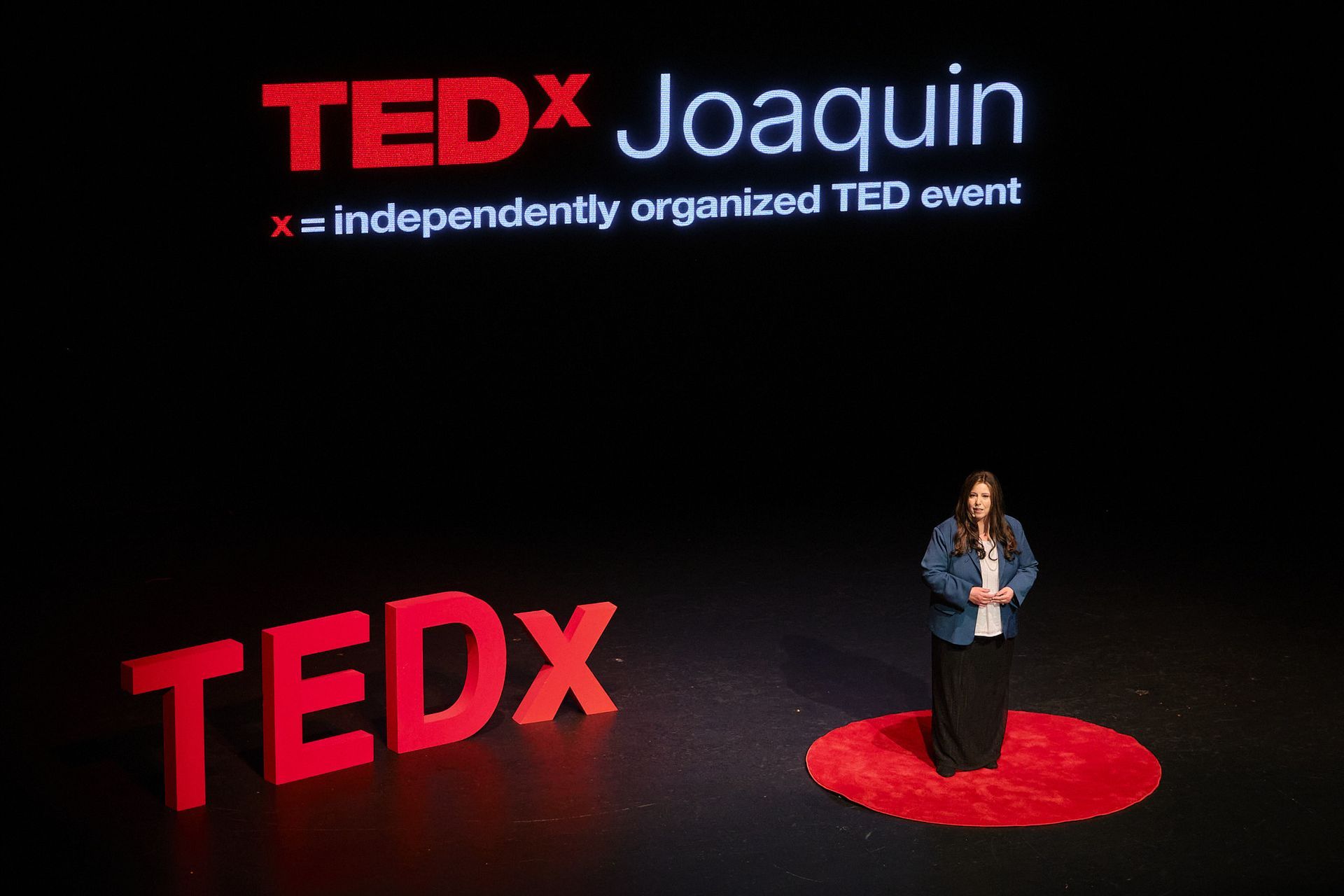 A person stands on a red circular rug on a dark stage with a large red 