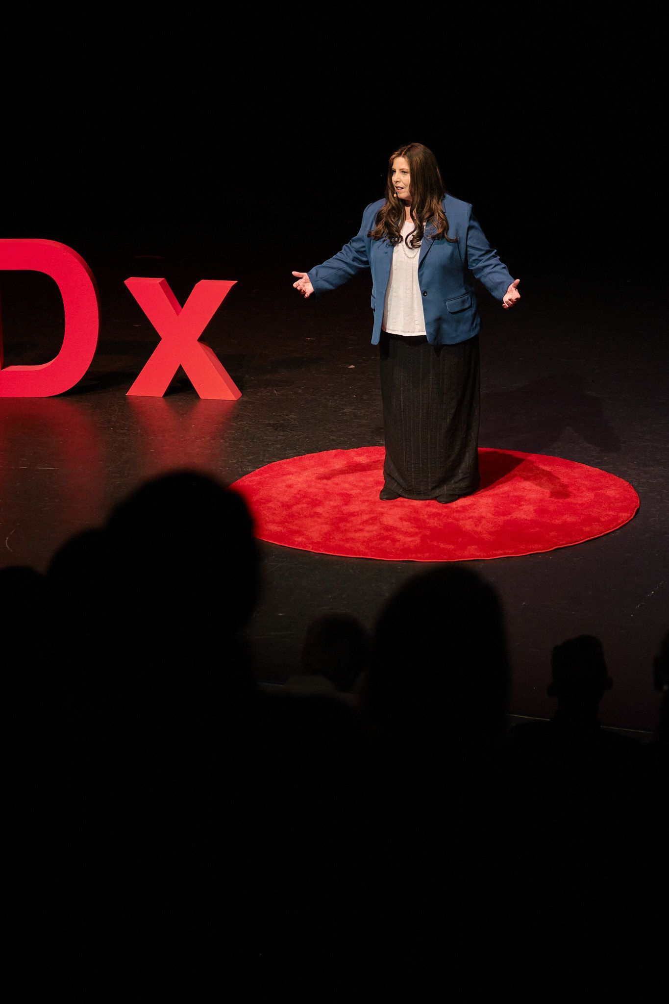 A speaker stands on a circular red rug on a stage next to a large red 