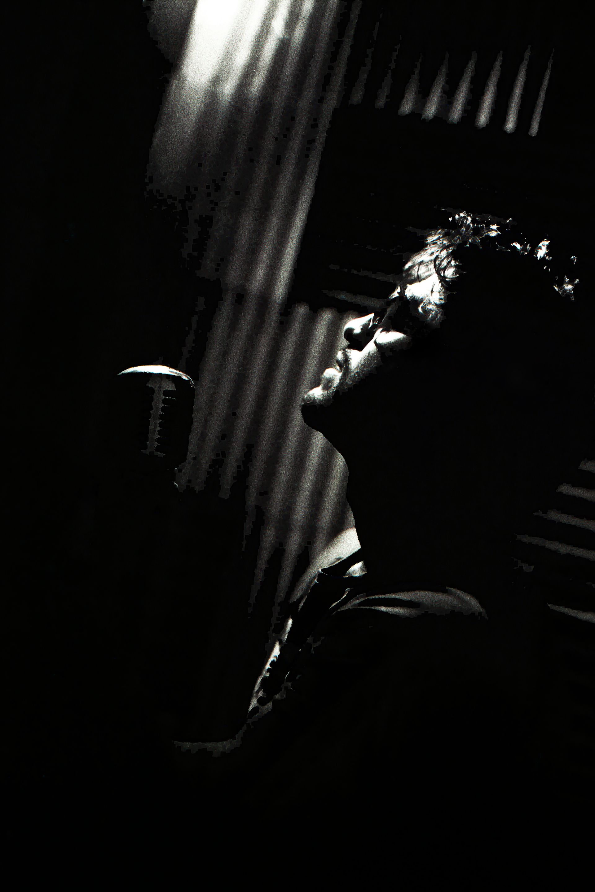A profile view of a person singing into a vintage microphone in a dark, moody setting with dramatic shadows.