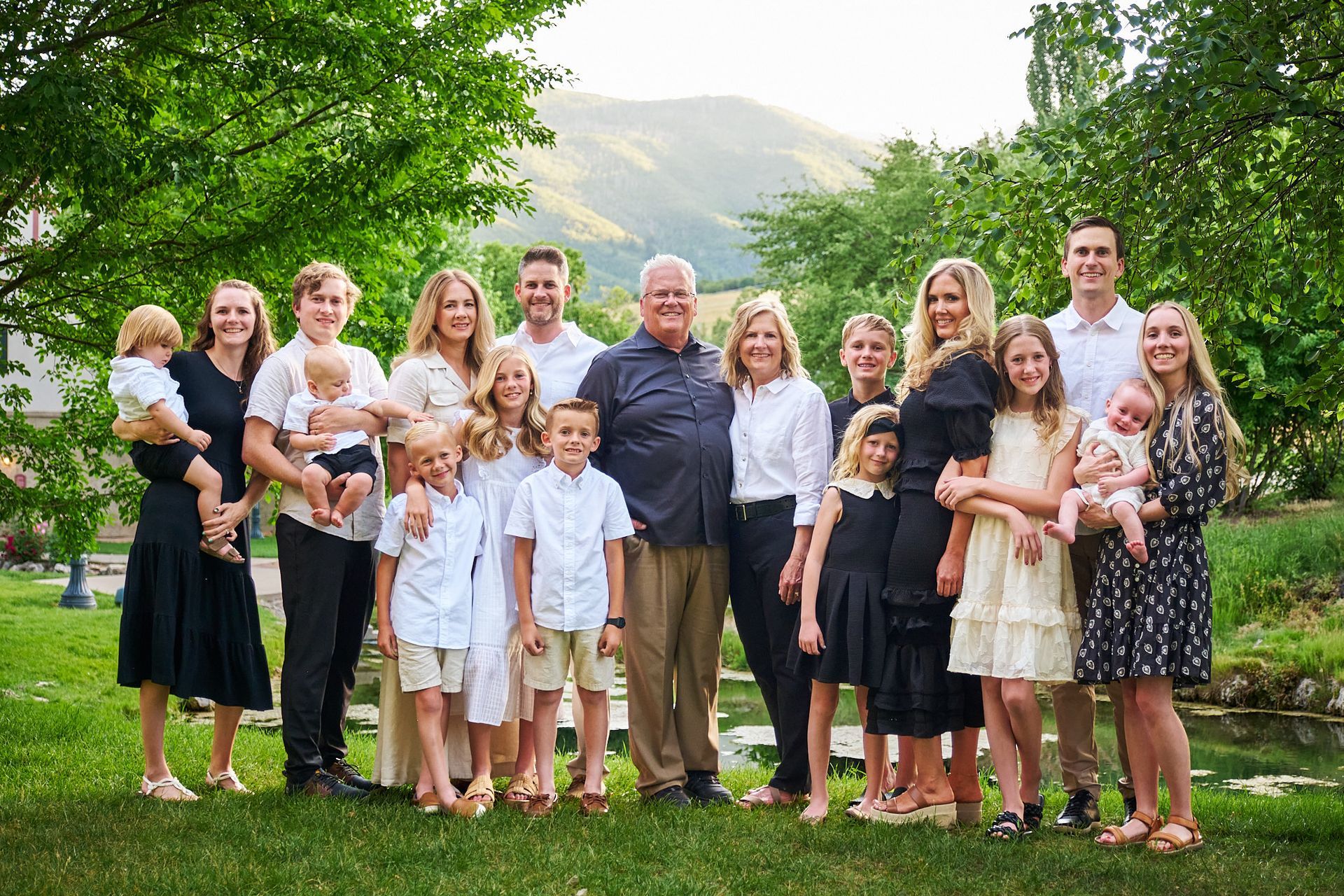 A large family poses for a formal portrait in a grassy park setting with a mountain backdrop.