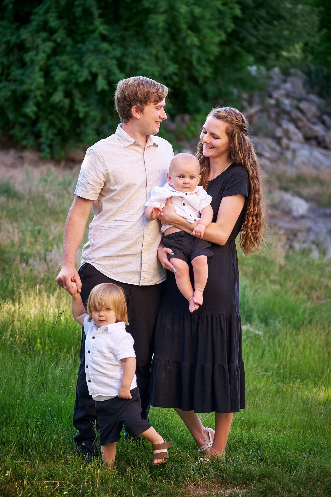 A family of four outdoors in a grassy field, posing together and smiling.