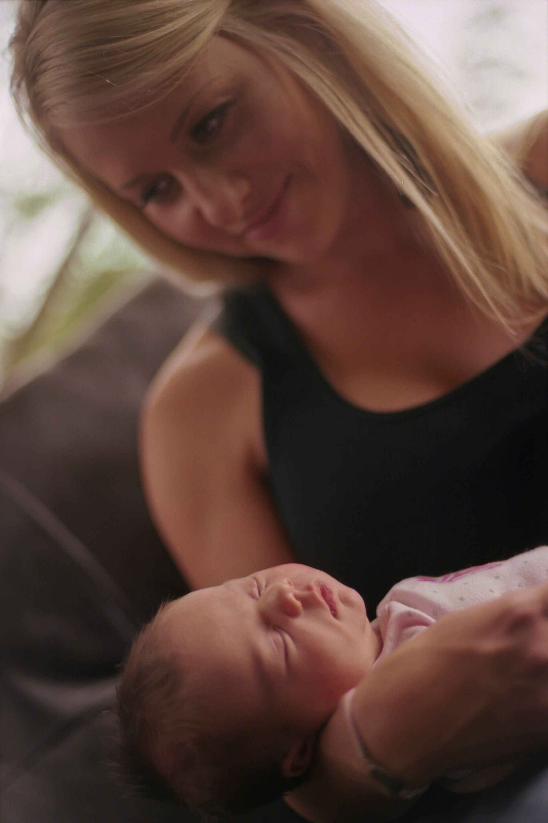 A person in a dark tank top looks down affectionately at a sleeping infant held in their arms.