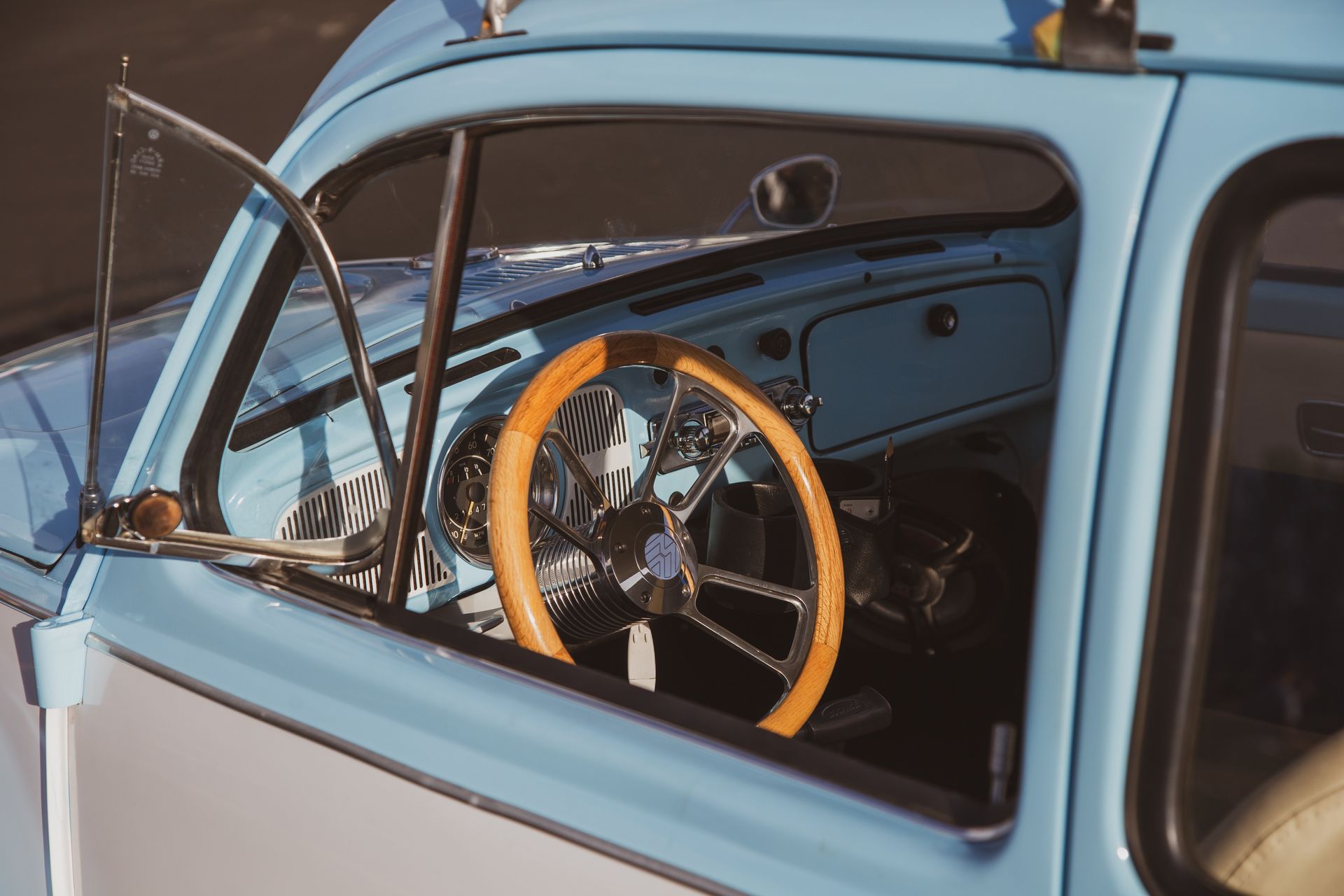 Interior view of a light blue vintage car featuring a wooden steering wheel and an open vent window.