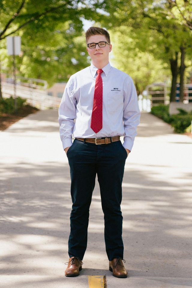 A person wearing a light shirt, red tie, and dark pants standing on a paved path outdoors with trees in the background.