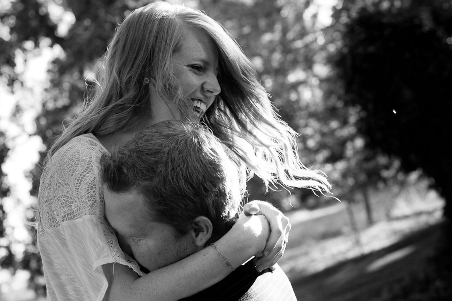 A young person smiles warmly while embracing another individual outdoors in a sunlit, black-and-white setting.