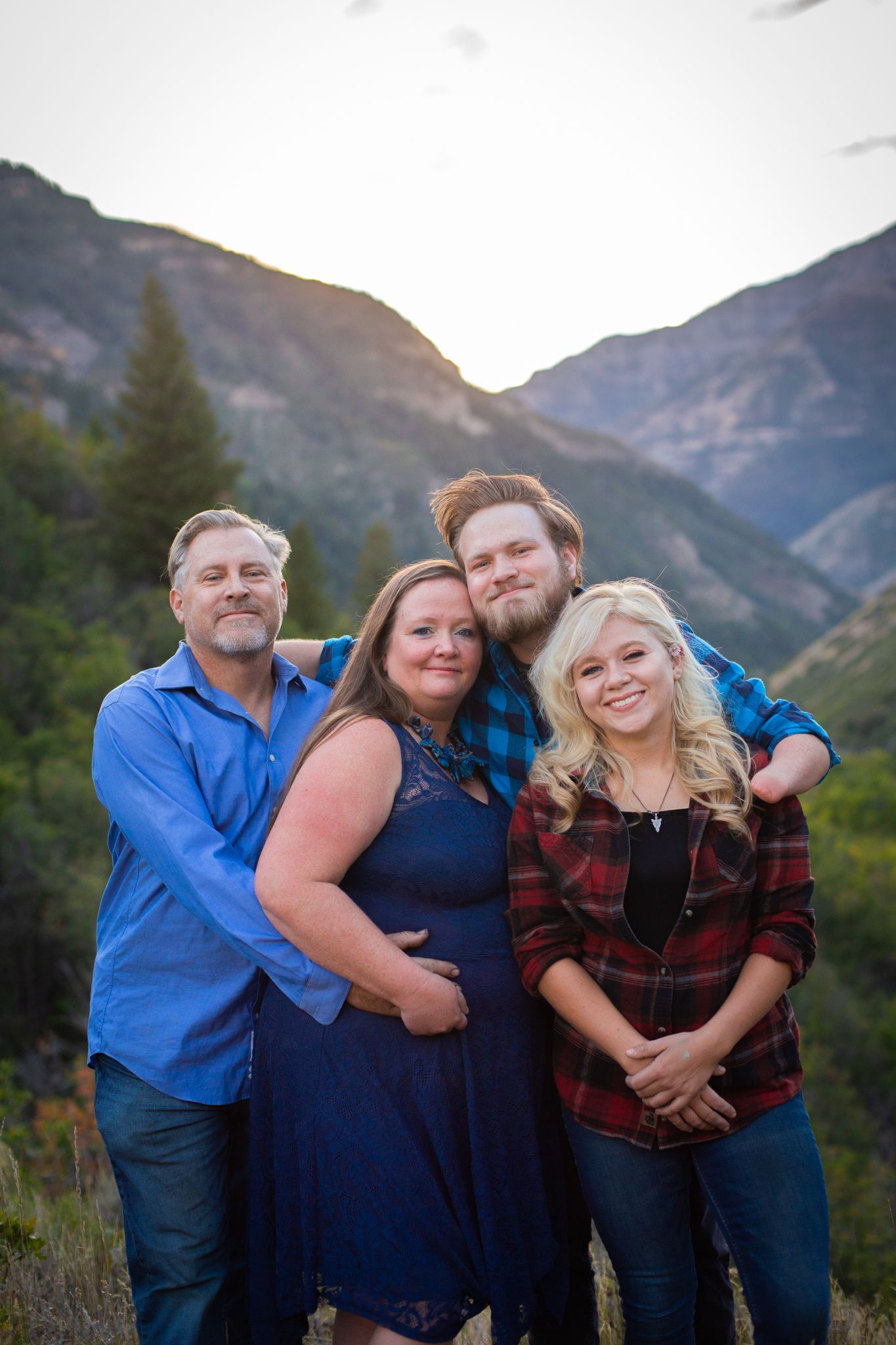 A group of four people pose together in a mountain setting at sunset, with a sunlit peak in the background.