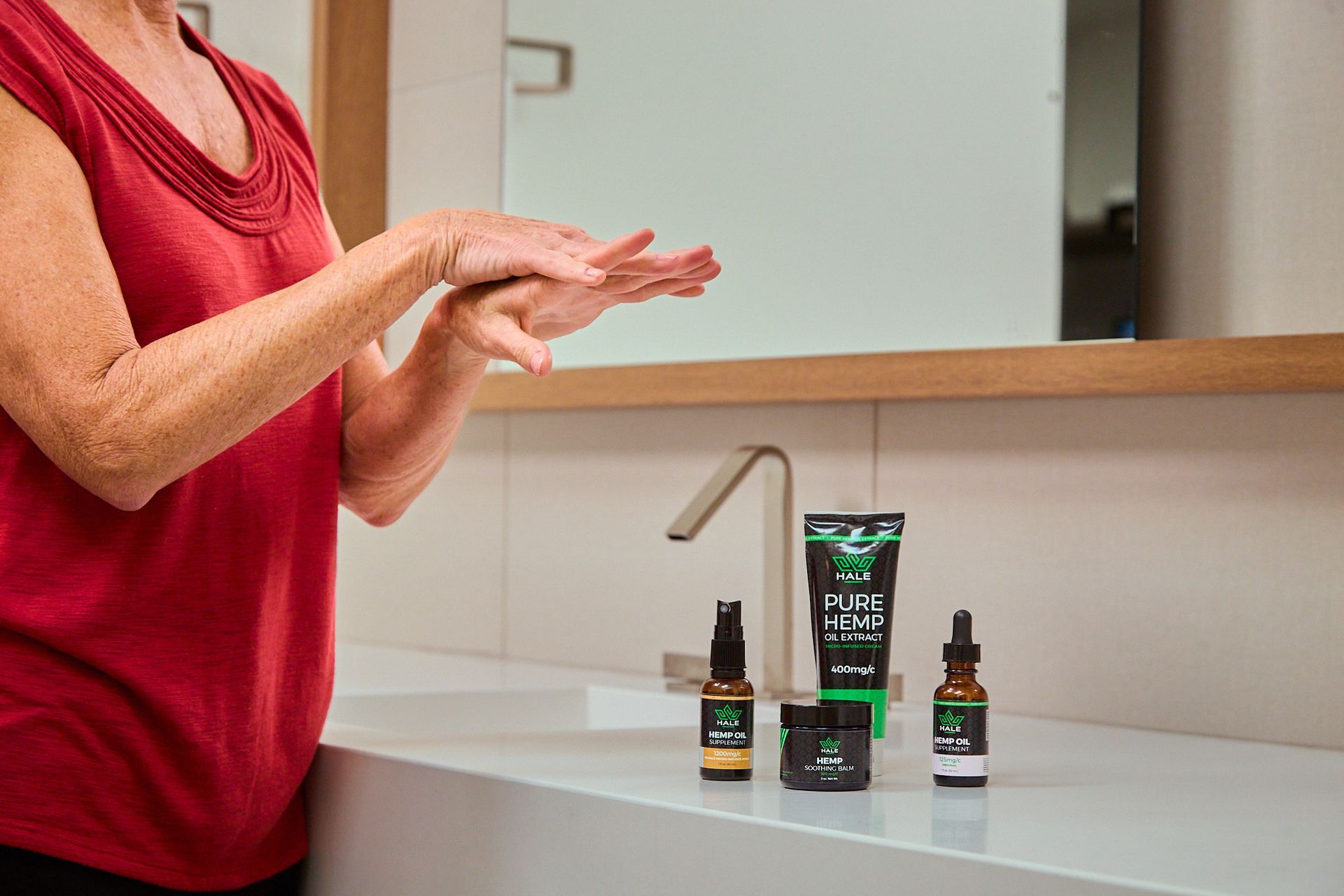 A person applying skincare product to their hands next to a set of matching skincare bottles on a white bathroom counter.