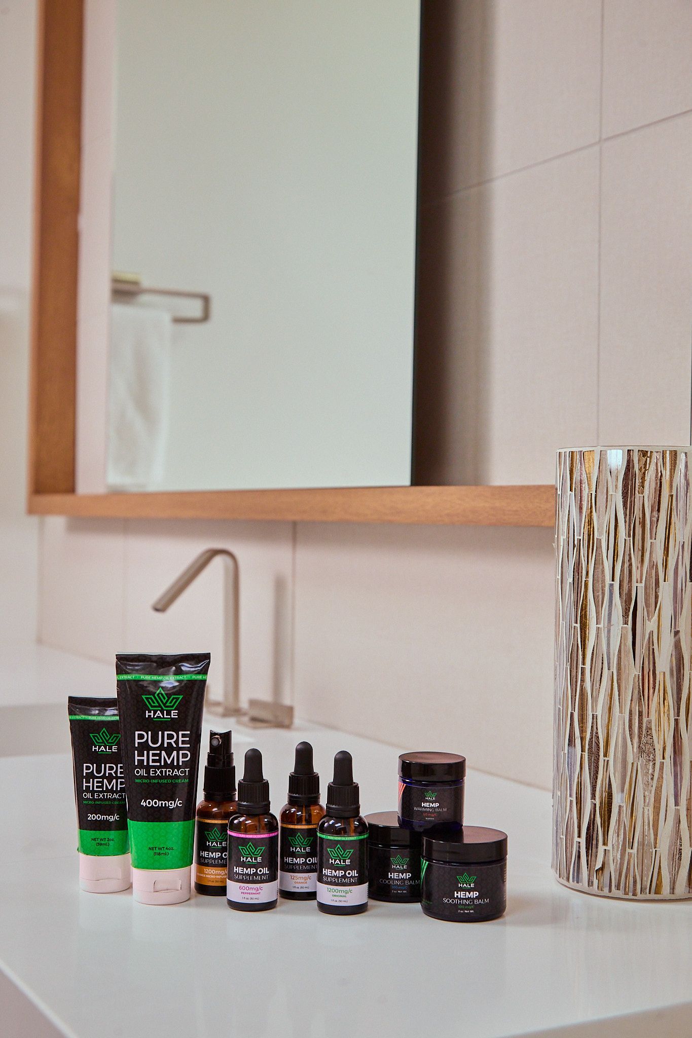 A collection of green and black skincare bottles and jars sits on a white bathroom vanity in front of a framed mirror.