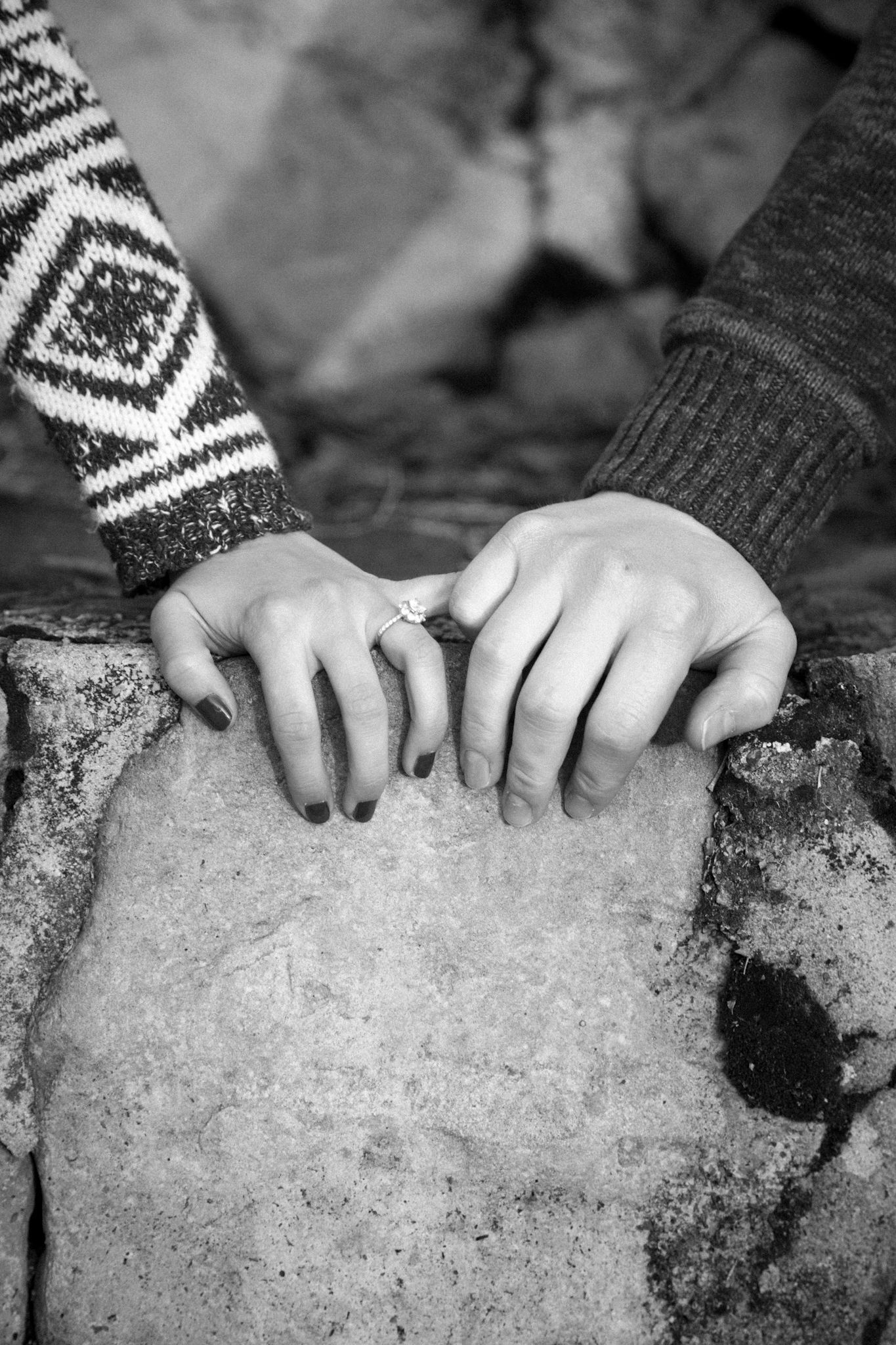 A close-up of two pairs of hands with patterned sleeves resting on a textured stone surface in black and white.