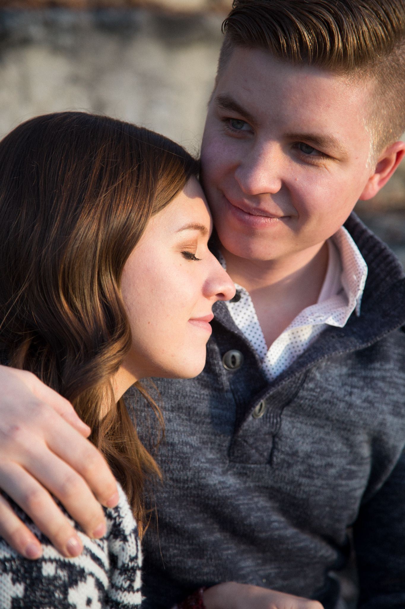 A man looking affectionately at a woman with her eyes closed, both wearing sweaters in a soft, natural setting.
