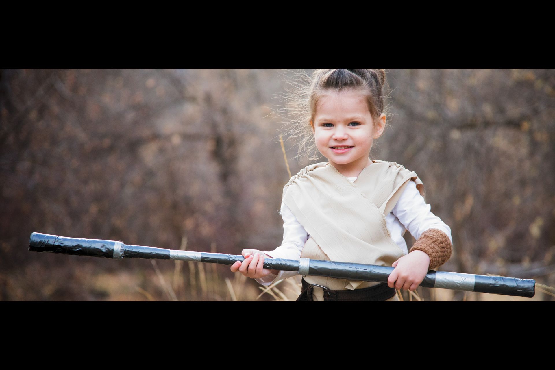 A child dressed as a Star Wars character holding a staff in a blurred outdoor setting.