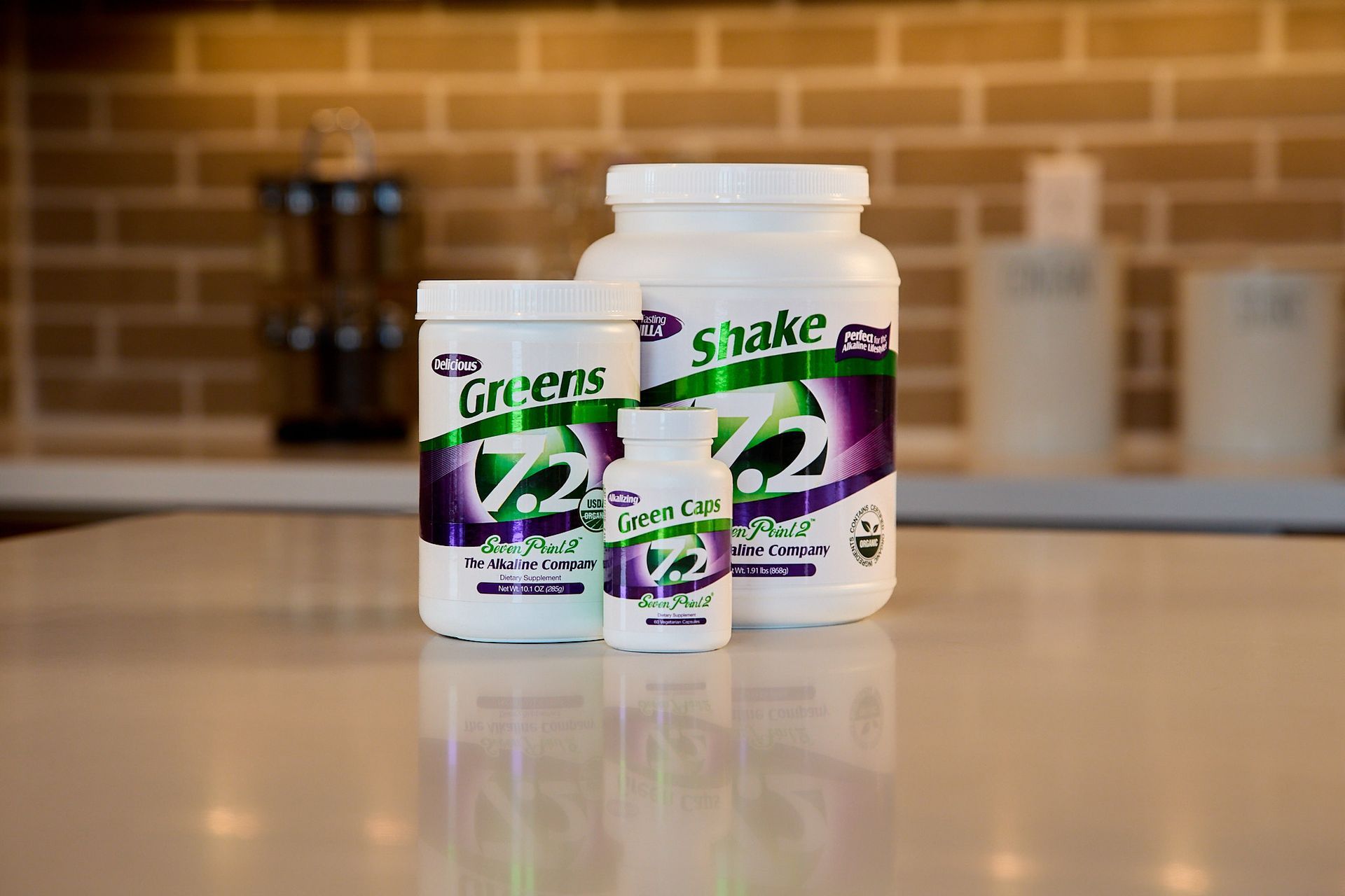 Three 7.2 branded nutritional supplement containers on a white counter in front of a brick-style kitchen wall.