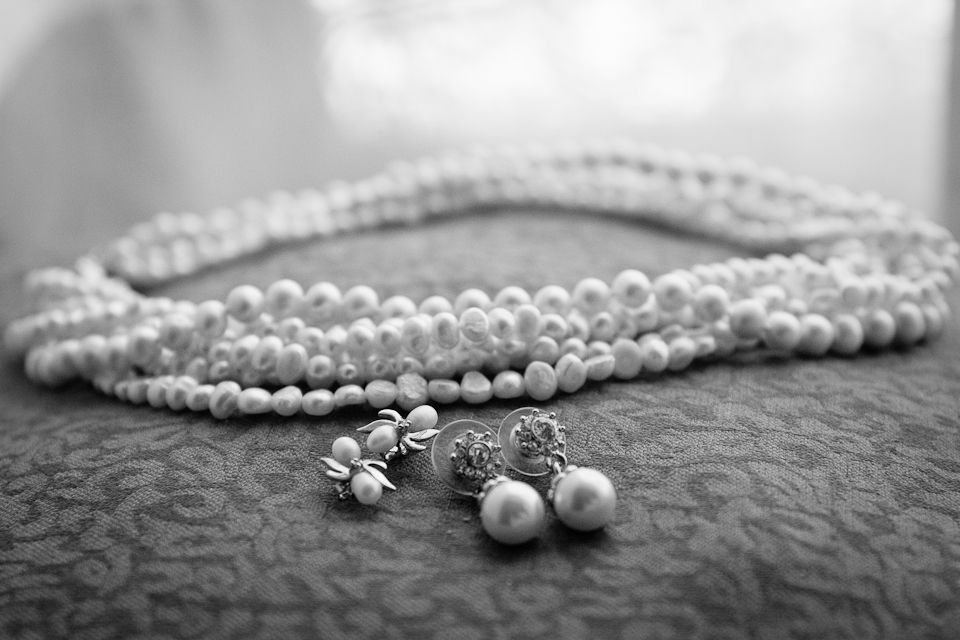 A multi-strand pearl necklace rests on a textured surface next to a pair of matching pearl stud earrings.