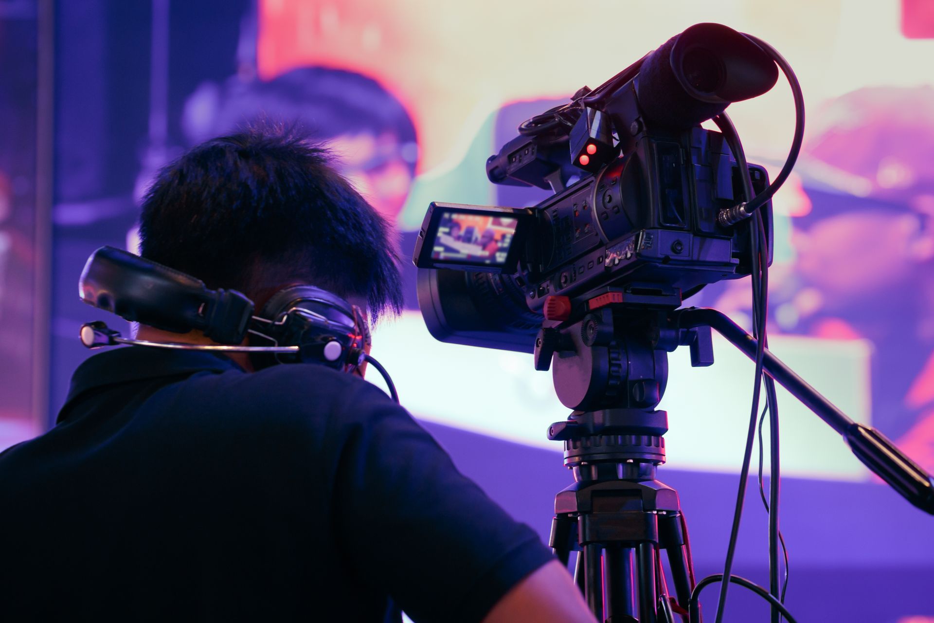 Person wearing headphones operates a video camera on a tripod.