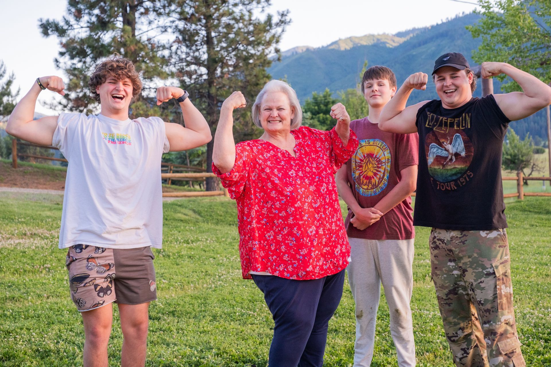 Three people flexing their biceps in an outdoor setting with a woman in a red shirt standing in the center.