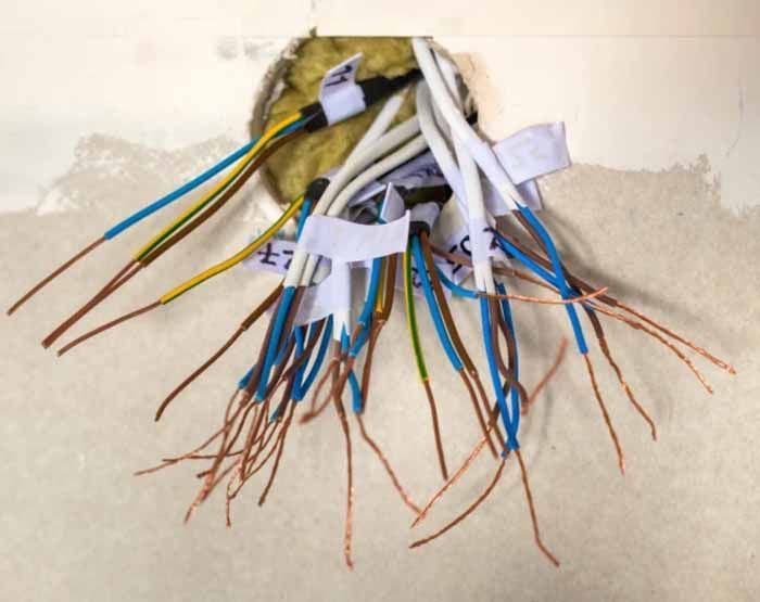 Bare electrical wires emerging from a wall cavity, labeled with white tape.
