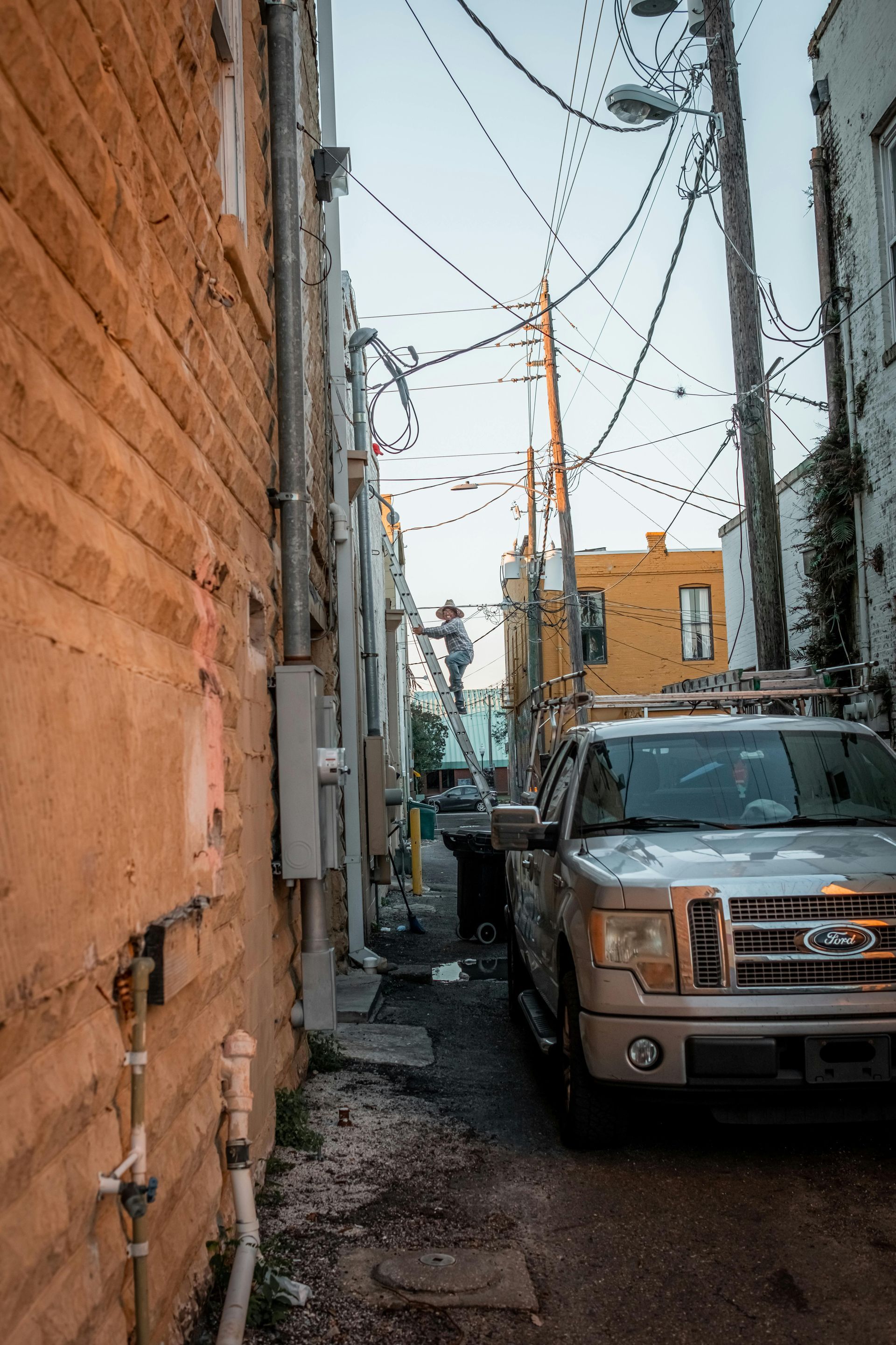 Narrow alley with parked truck, utility poles, wires, and buildings with a yellow one visible.