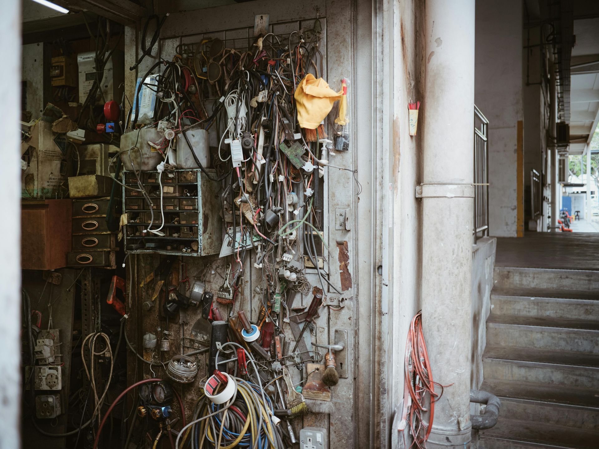 Workshop exterior: Tools and wires hang on a wall, a staircase leads to a building entrance.