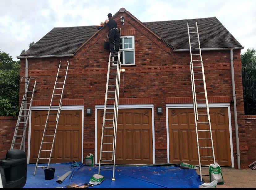 worker at the top of one of three ladders leaning against a house