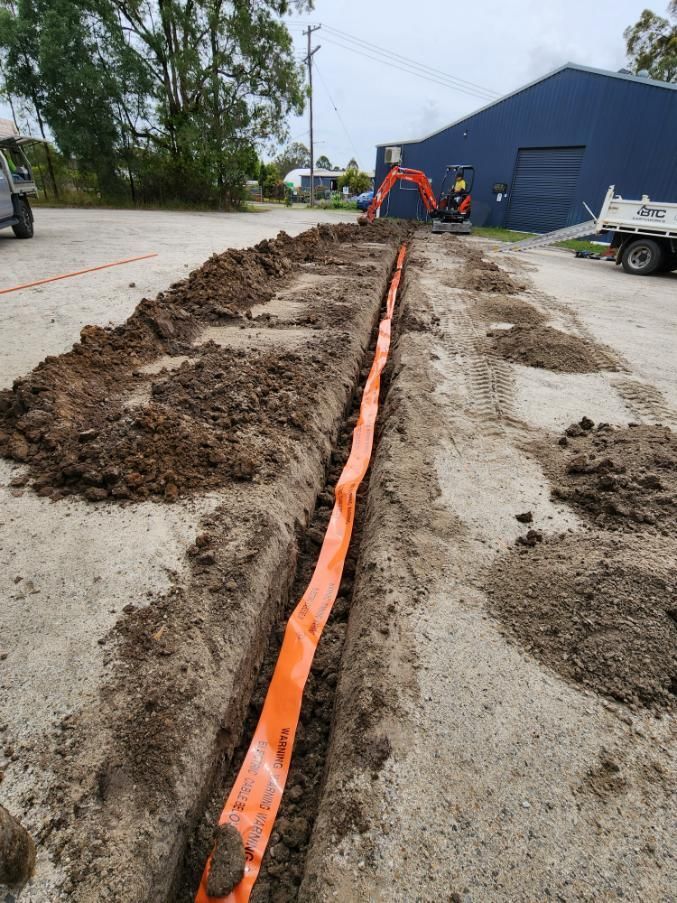 An Orange Pipe Is Being Installed In The Dirt In A Parking Lot — All Star Electrical Services in Austinmer, NSW
