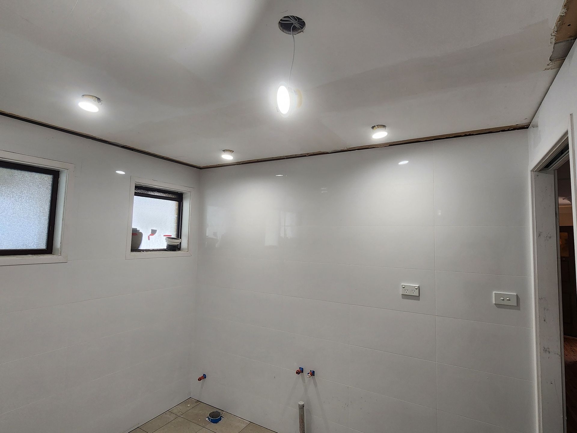 Bathroom With White Tiled Walls, Two Small Windows, and Recessed Lighting in the Ceiling