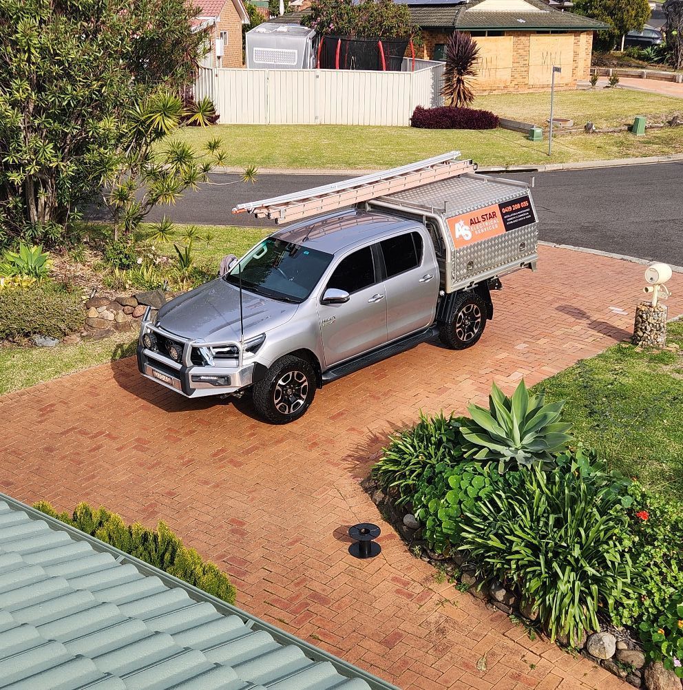 Silver Pickup Truck With a Ladder on Top Parked on a Red Brick Driveway