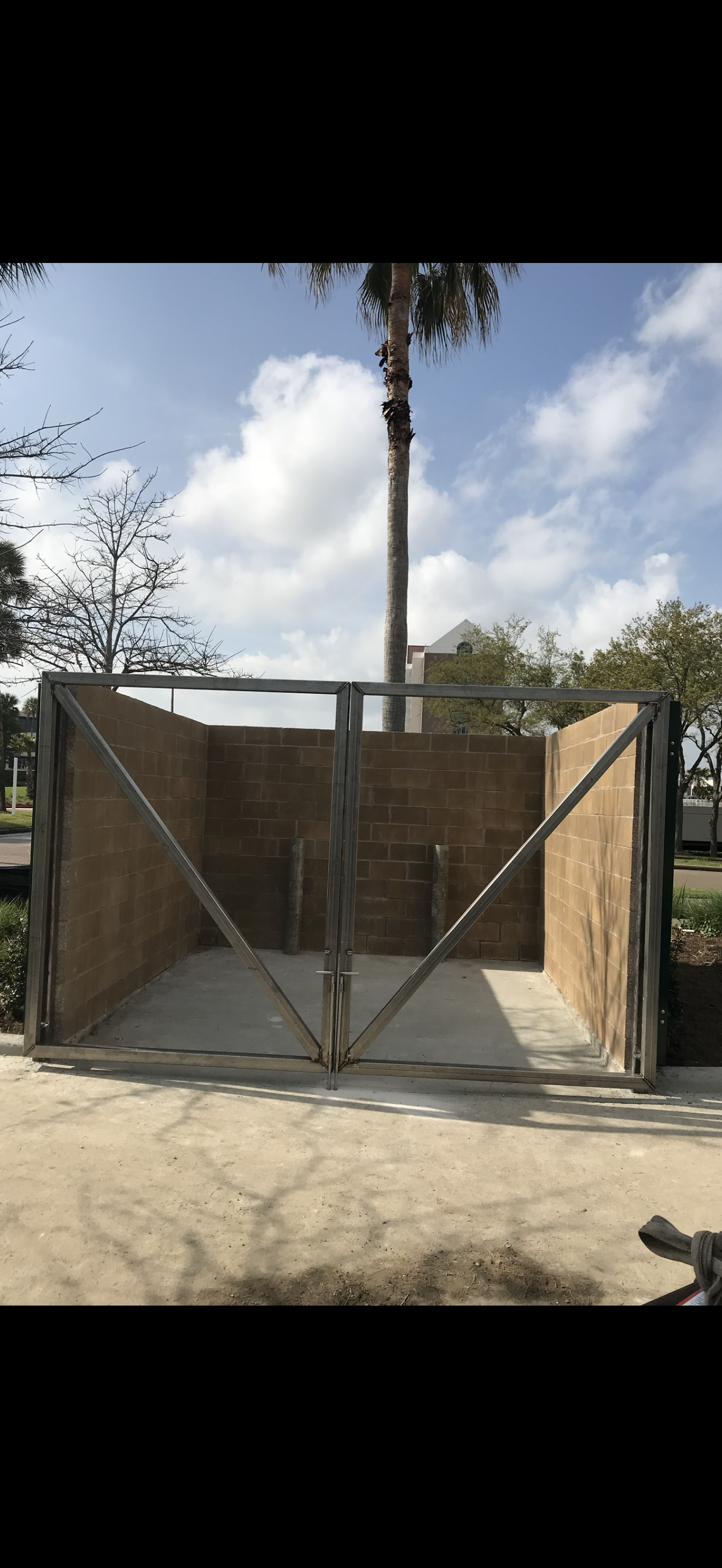A wooden structure with a gate and a tall palm tree in the background under a blue sky.