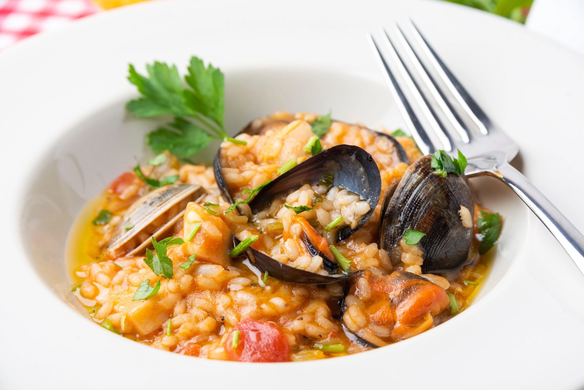 Una ciotola bianca colma di risotto ai frutti di mare, con vongole, cozze ed erbe aromatiche, servita con una forchetta d'argento.