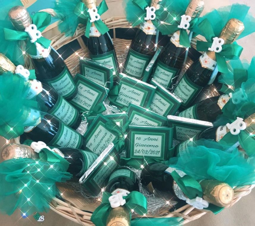 Un cestino di vimini pieno di piccole bottiglie con nastri verdi e scatoline abbinate con l'etichetta