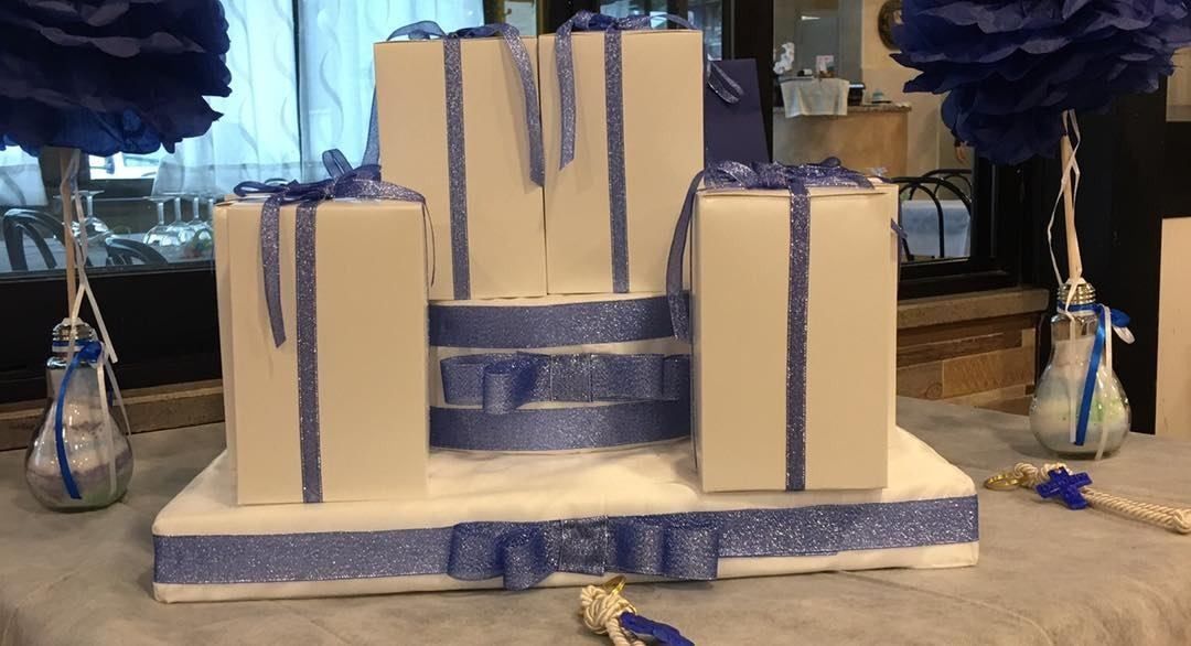 Tre scatole regalo bianche decorate con un nastro blu glitterato, esposte su una base coordinata con centrotavola floreali blu.