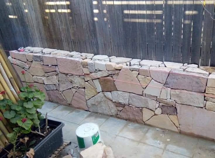A Stone Wall is Being Built on a Patio Next to a Fence — Queanbeyan East, NSW — Traditional Stone Structures