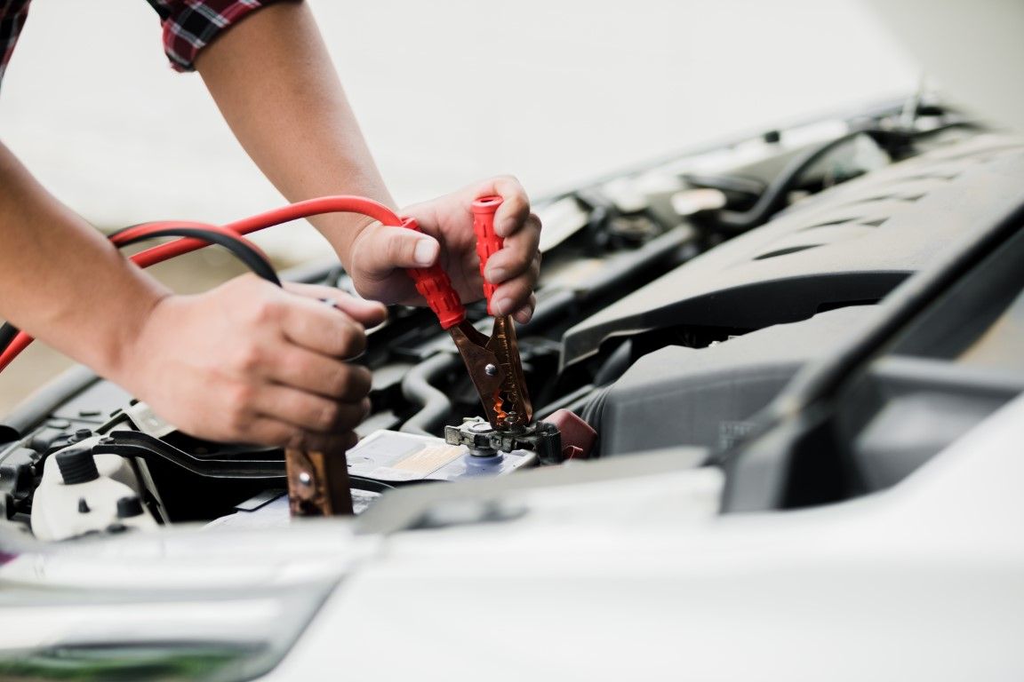 Hands connecting jumper cables to a car battery in an engine bay. Red and black cables.