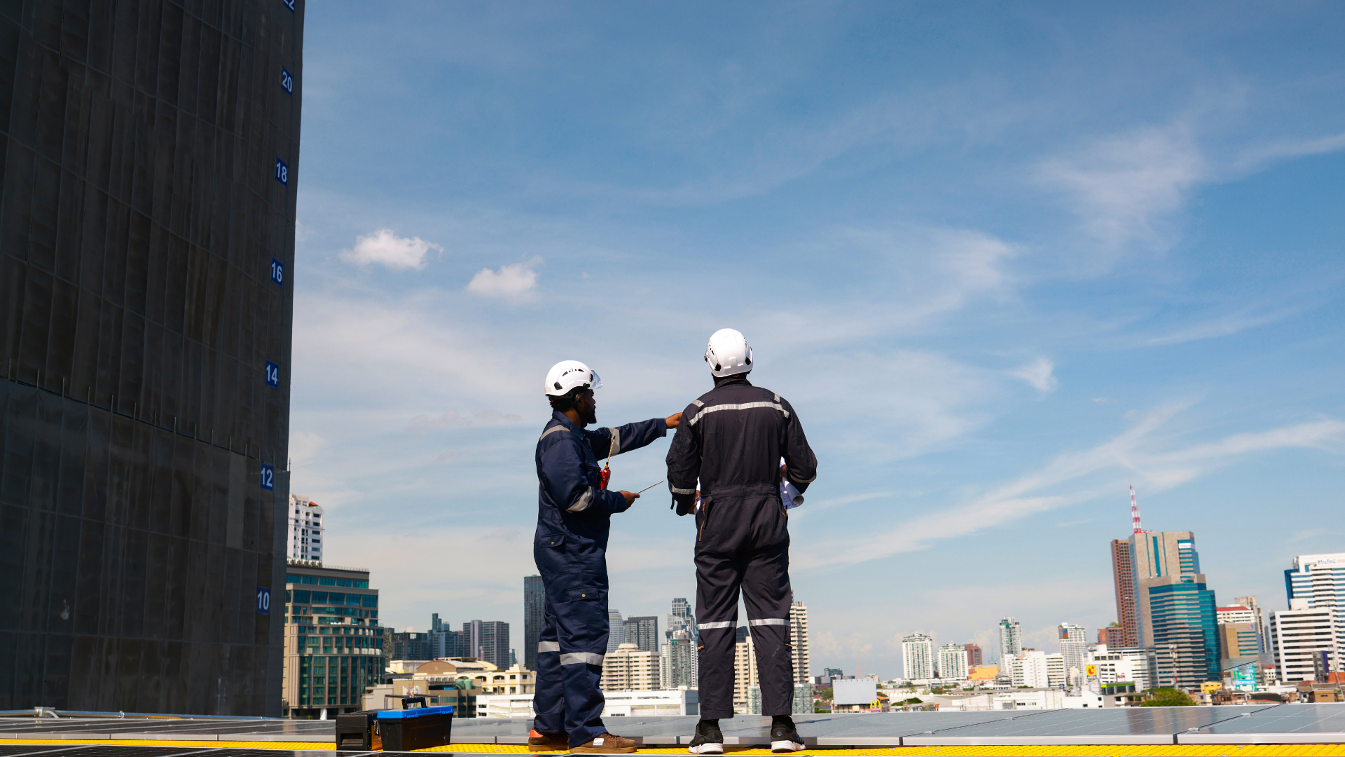 Two construction workers are standing on top of a building talking to each other.