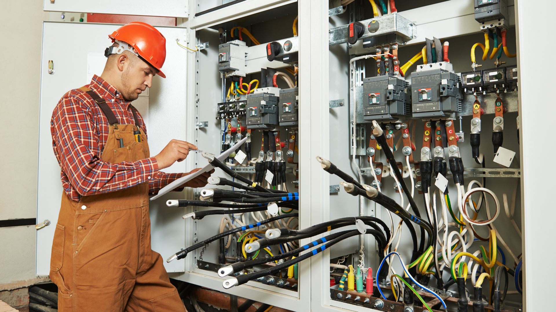 A man wearing a hard hat is working on an electrical box.